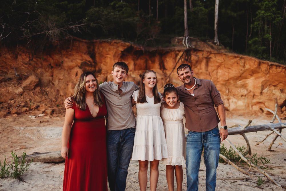 Family group poses together on rocky beach with orange cliffs in background.