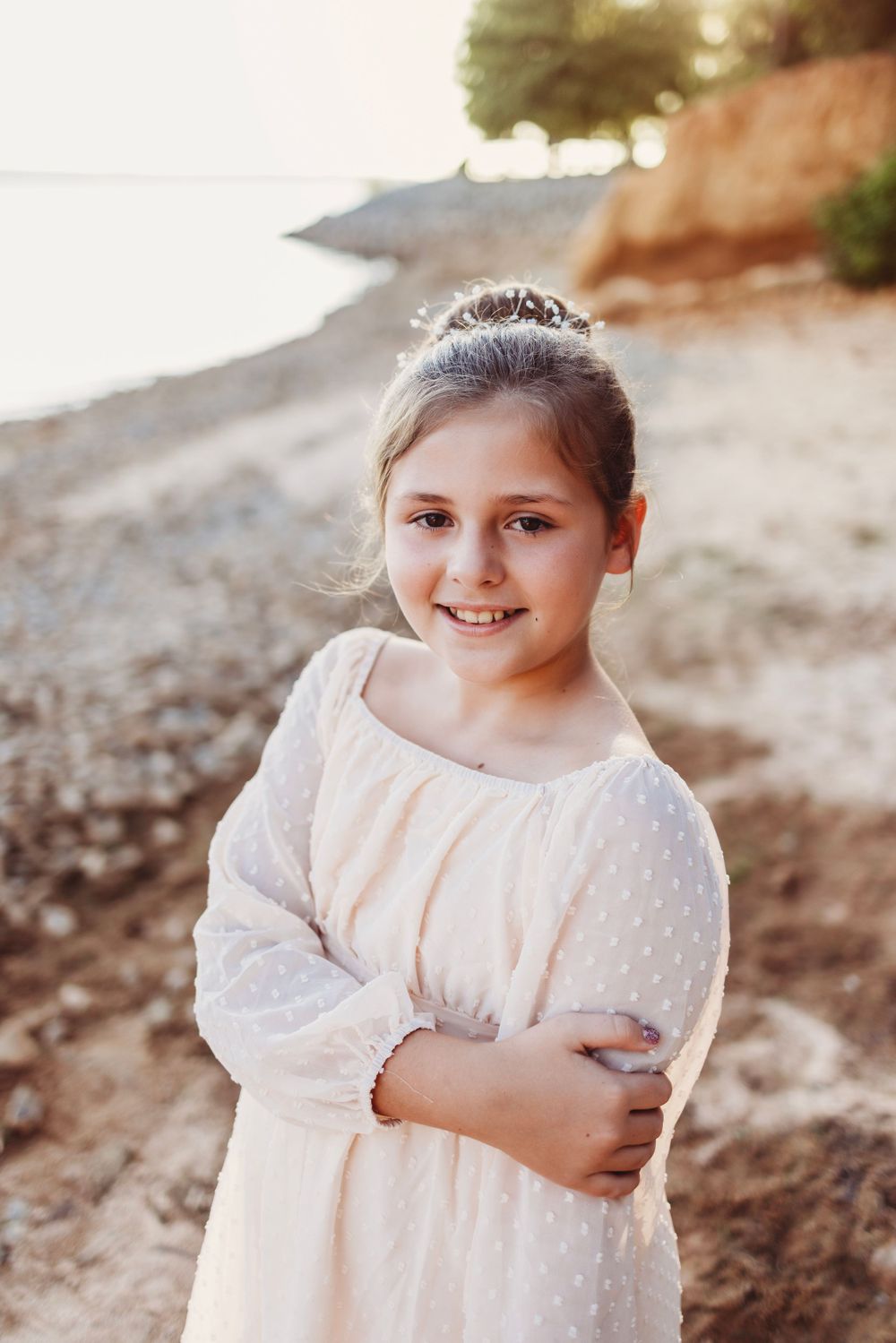 Young person in white dress wearing tiara poses on beach during sunset.