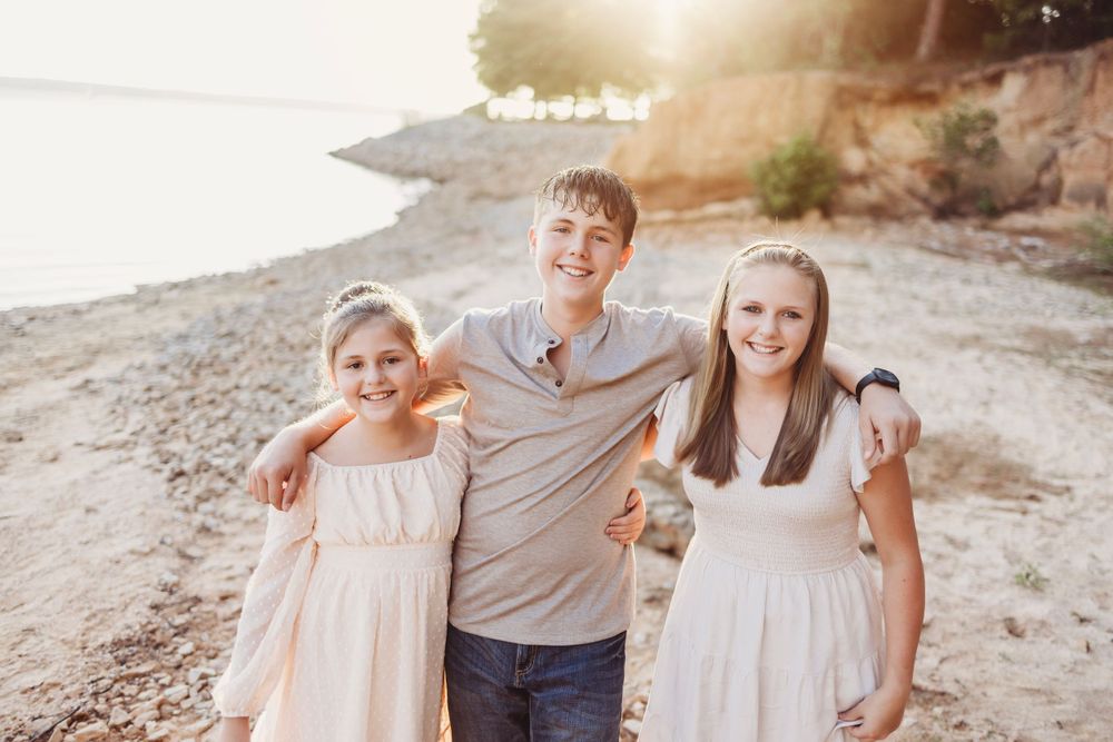 Three people pose together on rocky beach during sunset.