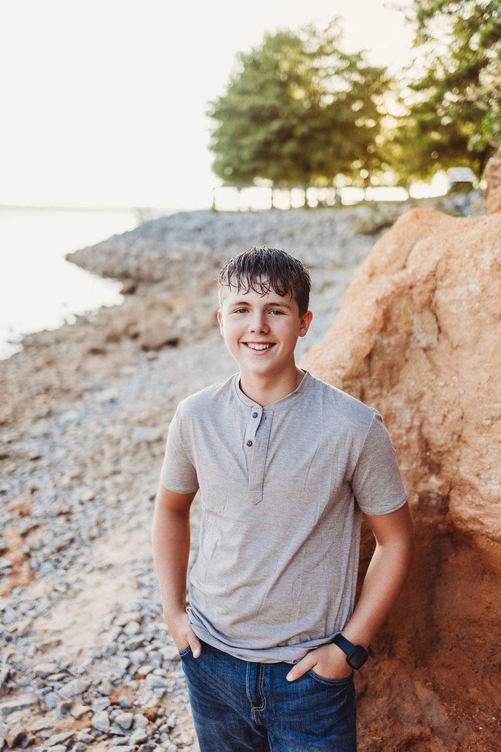 Portrait of a person in a grey shirt against a rocky cliff backdrop near water.