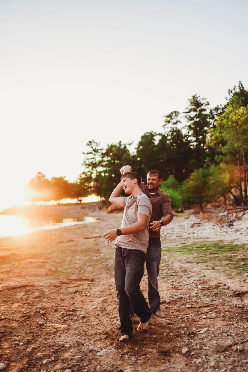 Two people sharing a playful moment on a rocky beach at sunset.