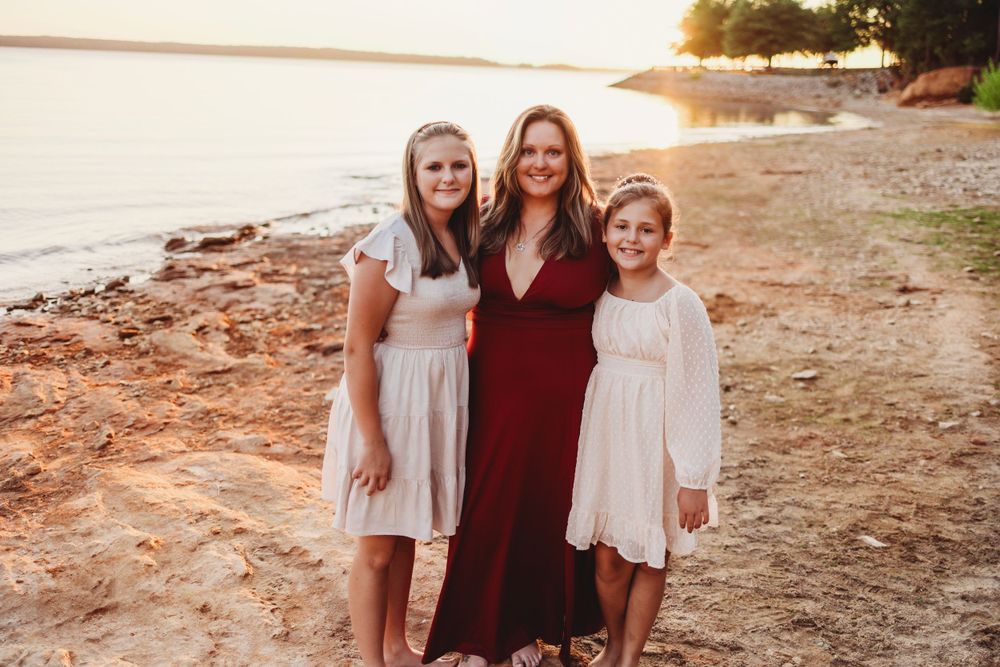 Three people in coordinated outfits pose for a family photo on a beach at sunset.
