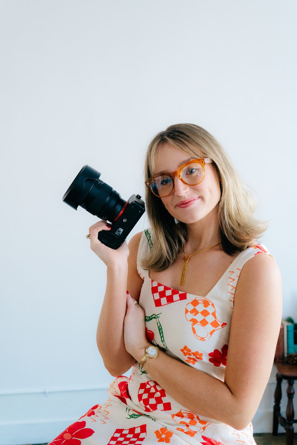 Creative portrait showing photographer with camera wearing orange patterned dress and glasses.