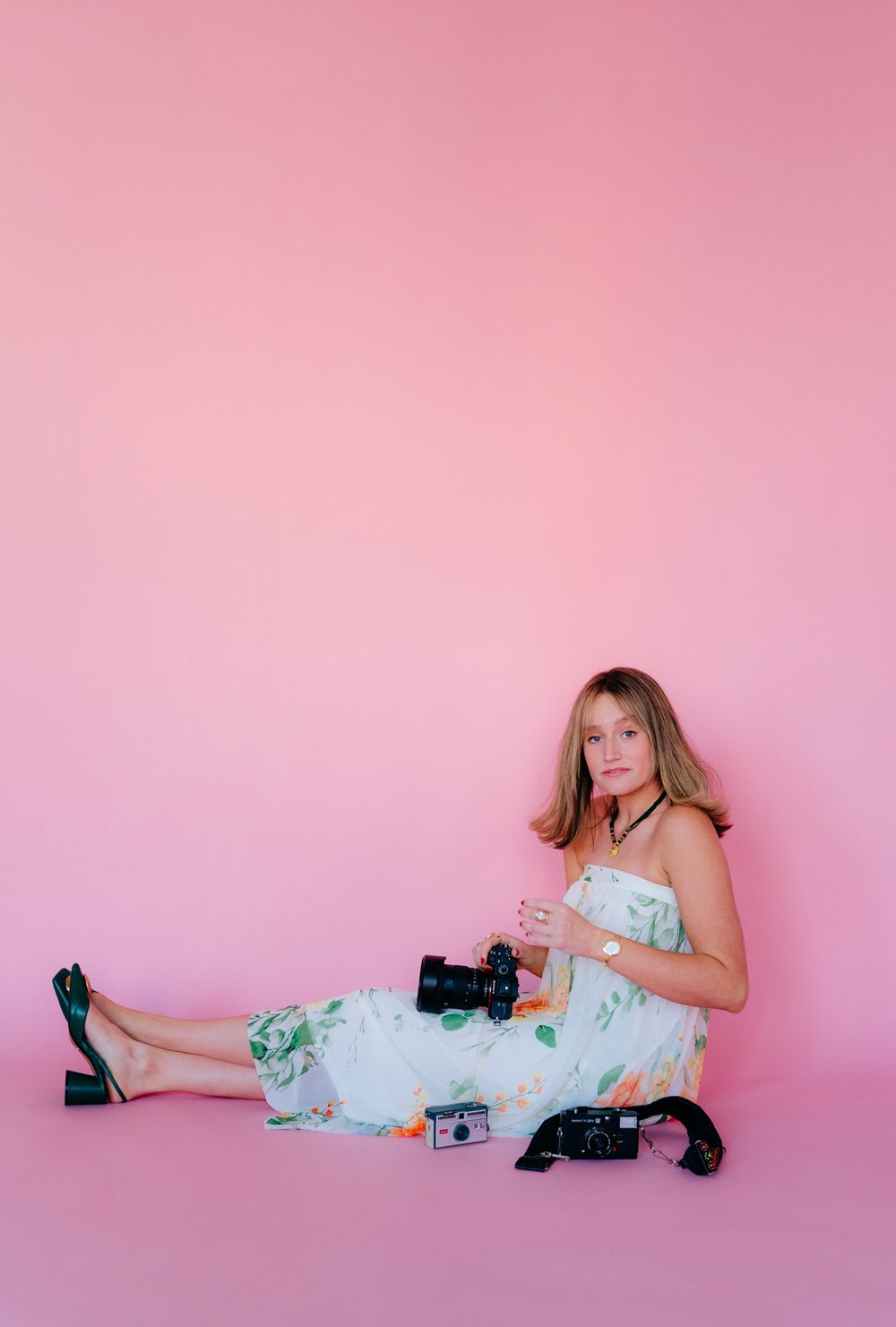 Portrait session with camera equipment against pink backdrop featuring floral dress and black shoes.