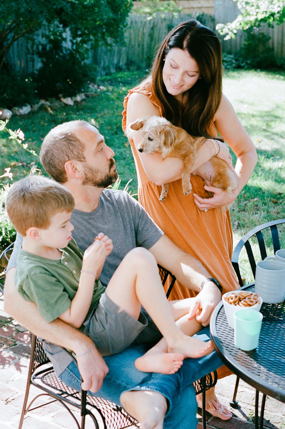 Family enjoying outdoor time with golden retriever puppy on patio furniture.