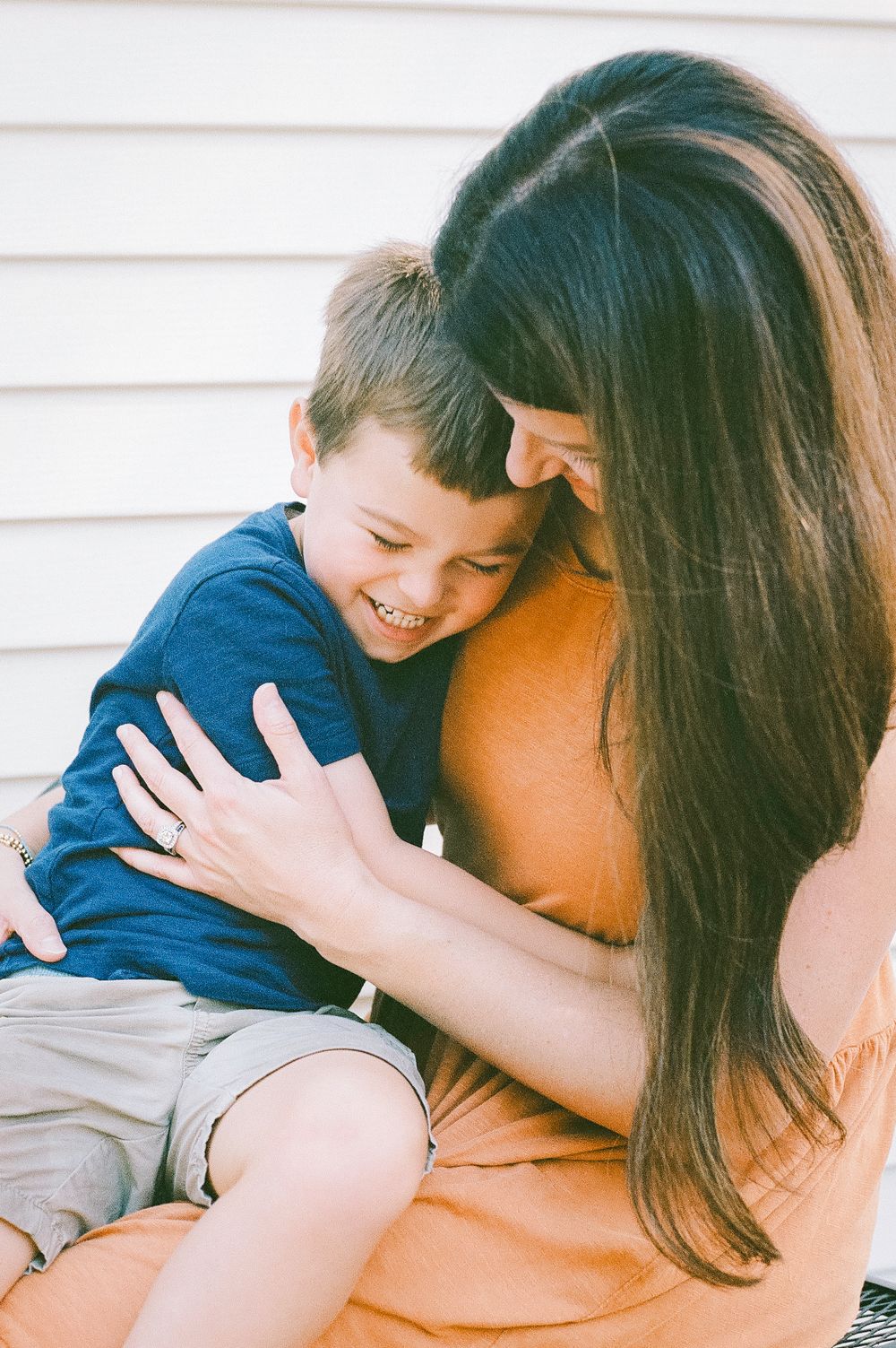 A sweet embrace shared on a sunny afternoon against white siding.