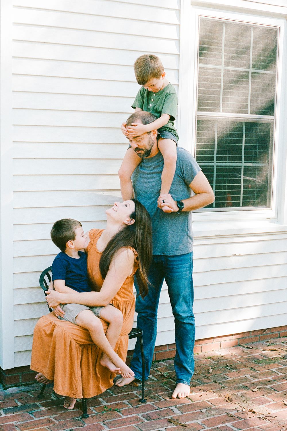 A joyful family moment captured outside their white house on a brick patio.