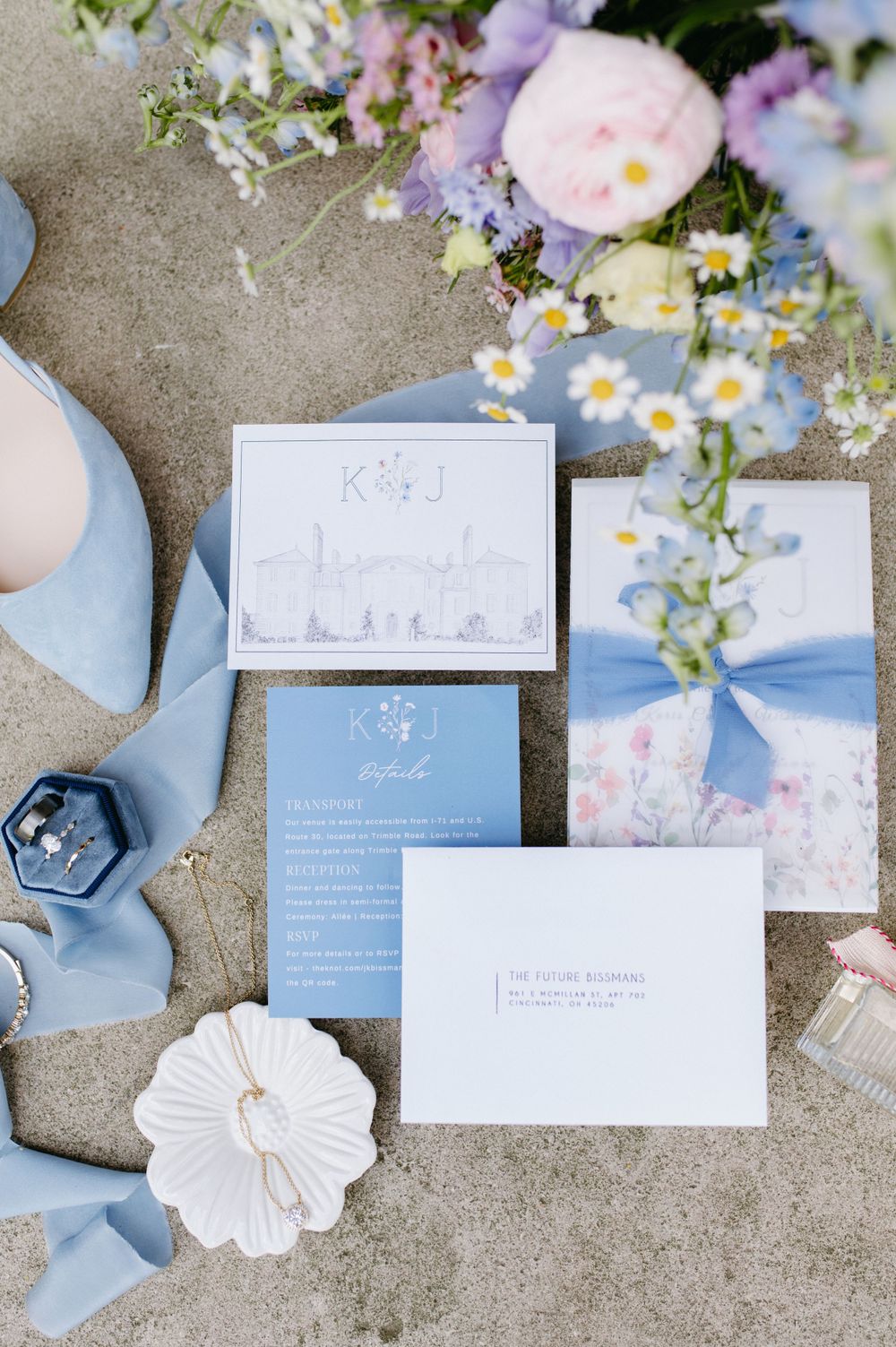 Light blue wedding stationery suite with floral accents and silk ribbons arranged on a textured surface.