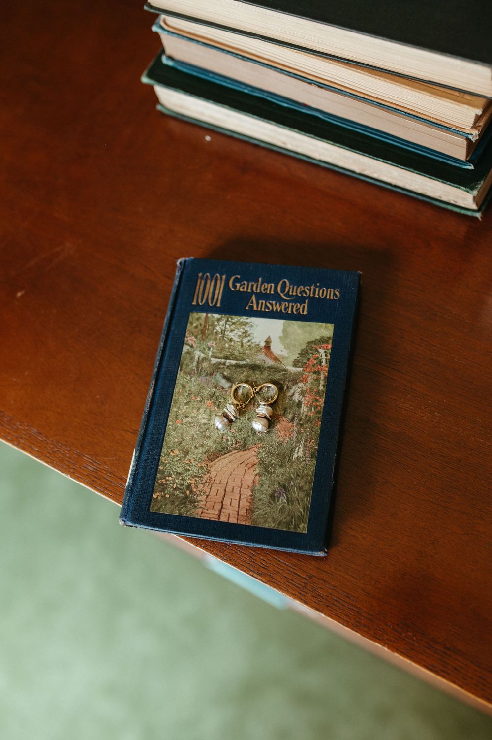 A vintage blue book titled '1000 Garden Questions Answered' resting on a wooden surface with other books stacked above.