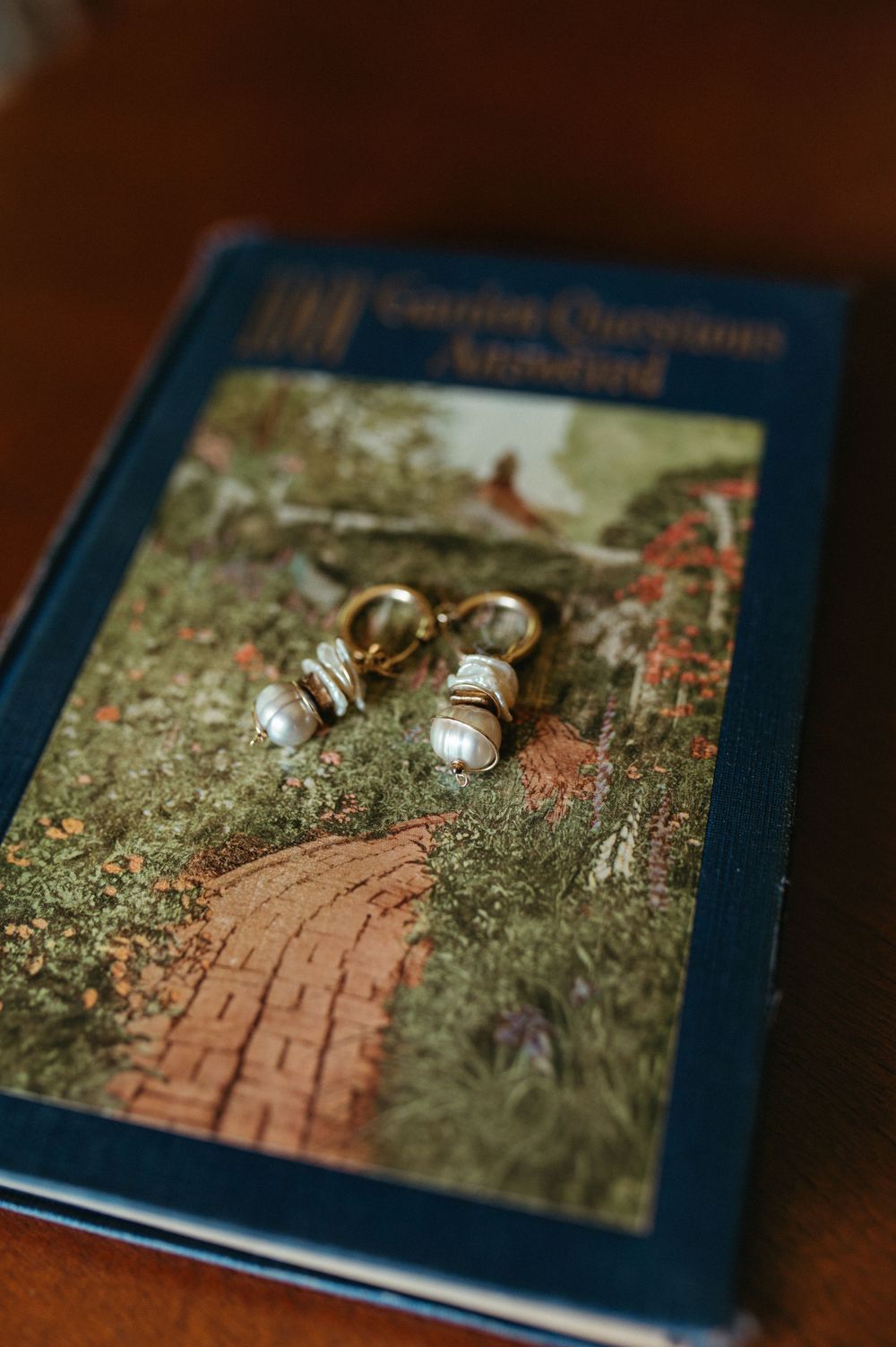Pearl earrings displayed on a blue book cover featuring a garden path illustration.