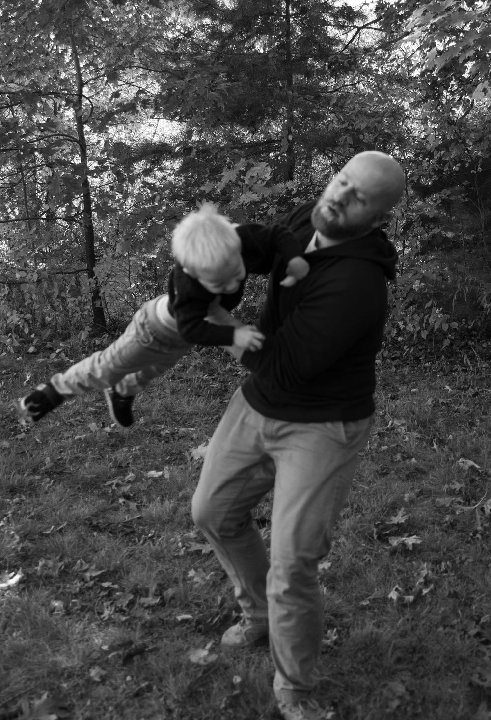 Father playfully swinging toddler son in black and white forest photo.