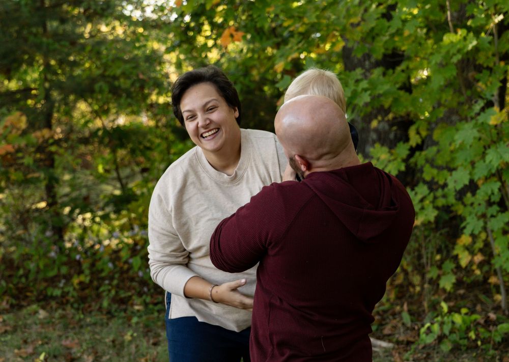 Laughing couple holding hands together outdoors among green autumn trees.