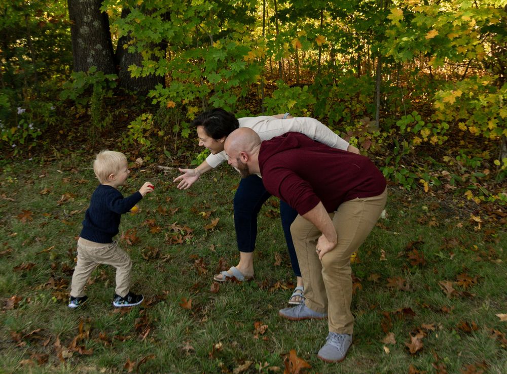 Parents bending down to greet their toddler son in autumn woodland setting.