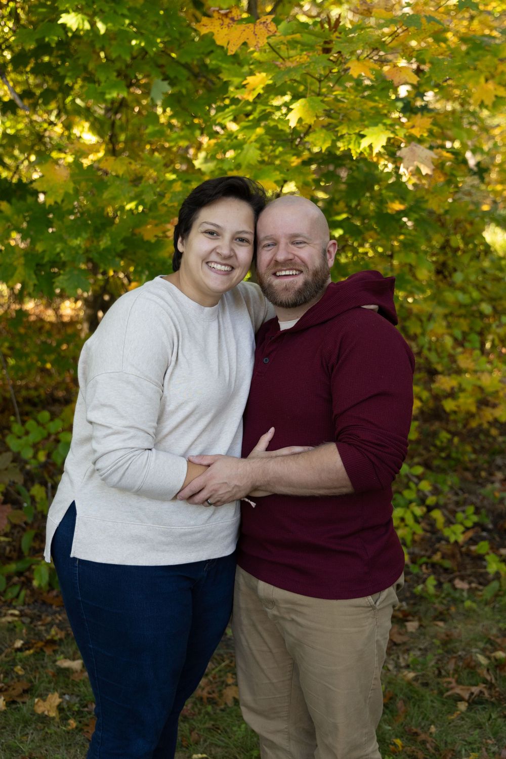 Happy couple embracing and smiling together outdoors with vibrant autumn foliage in background.