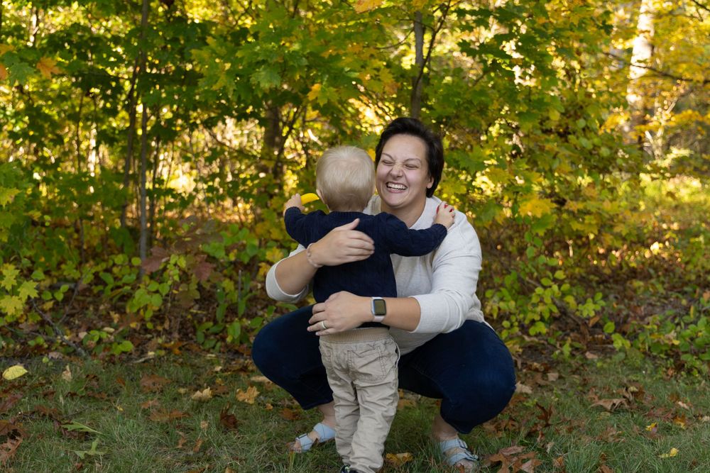 Happy mother hugging toddler son outdoors surrounded by vibrant yellow and green fall foliage.