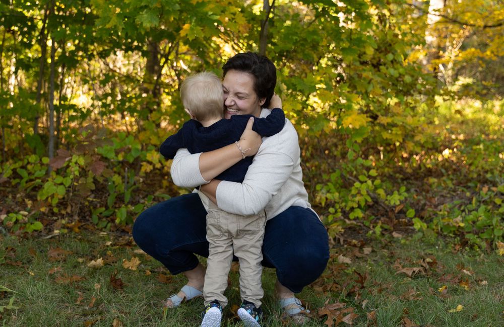 Woman hugging young toddler child in warm embrace outdoors during fall family photo session.