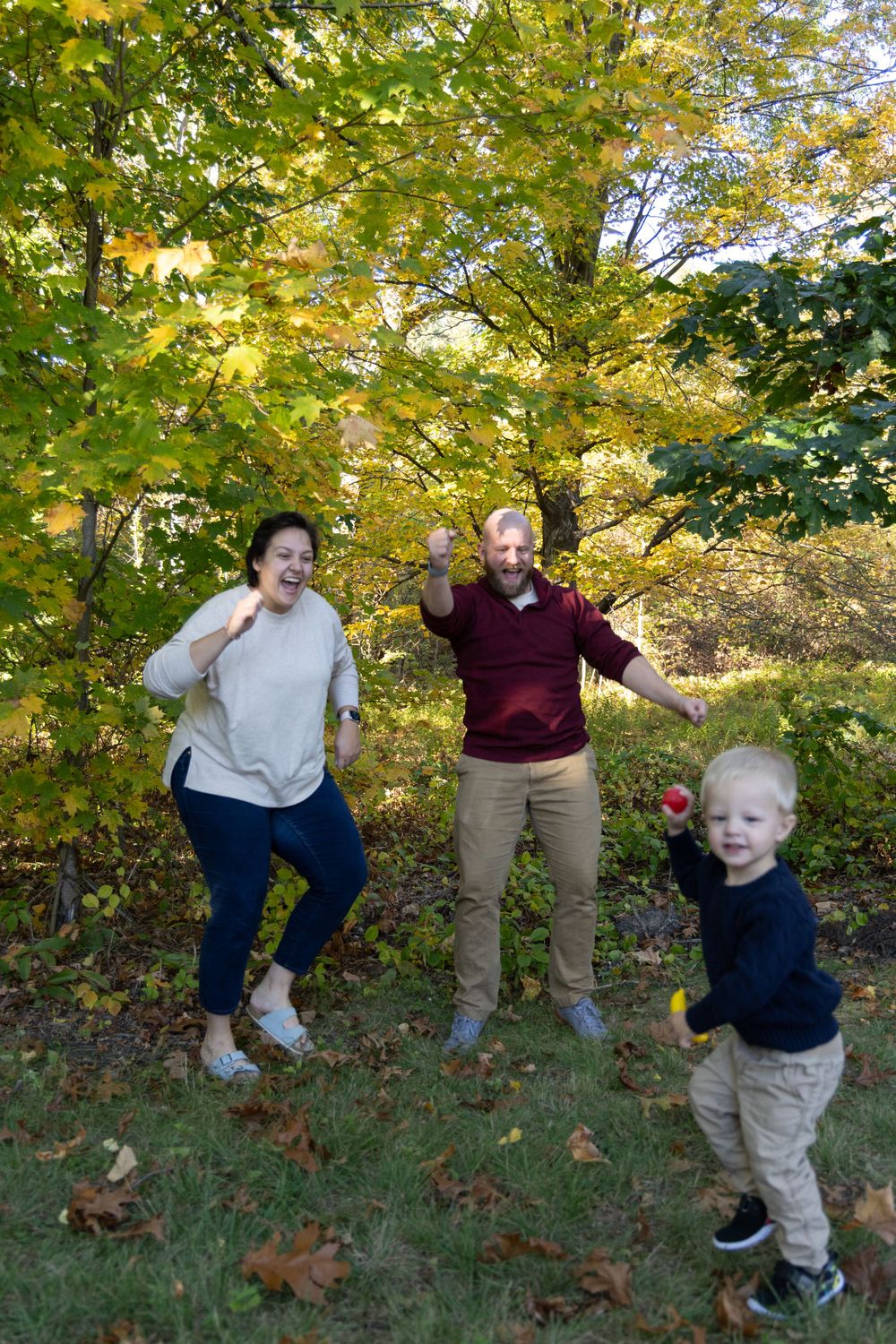 Excited family of three celebrating outdoors with toddler in fall foliage.