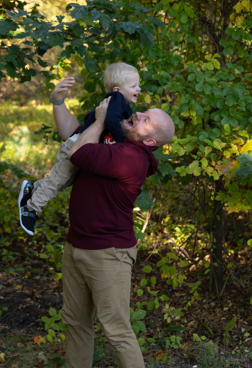 Father lifting joyful toddler high in the air in autumn park.