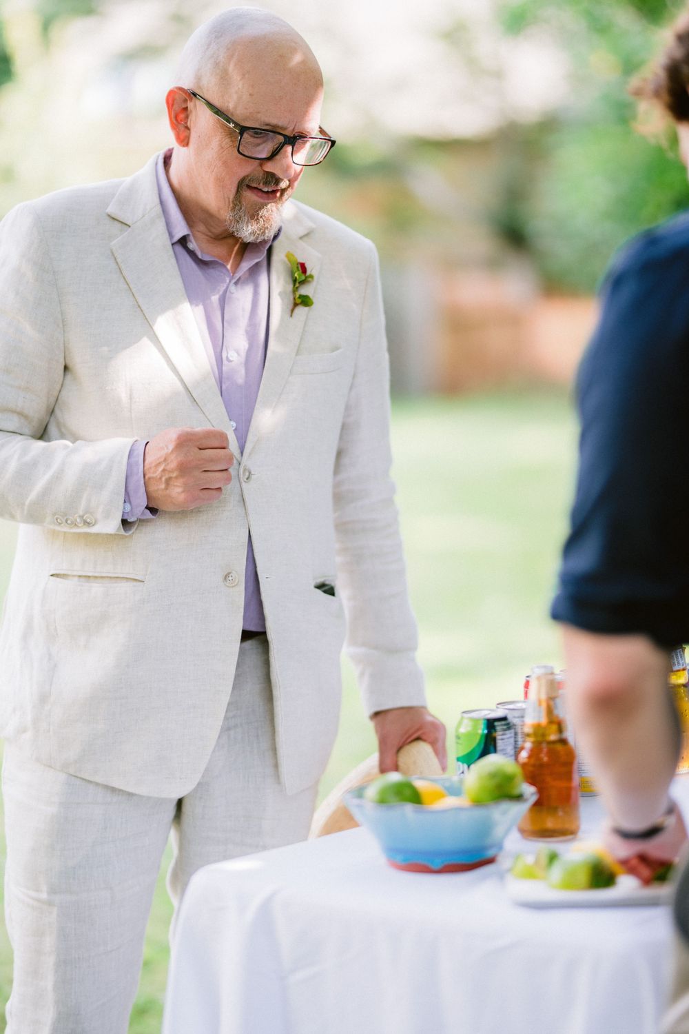 A guest in a light-colored suit enjoying refreshments at an outdoor garden party event.