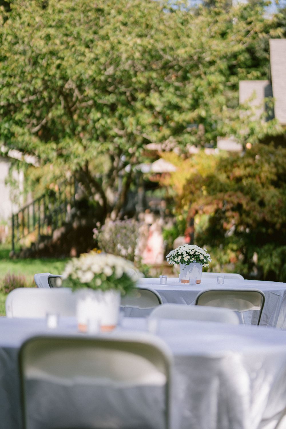 White-clothed tables set up outdoors with folding chairs and floral centerpieces.