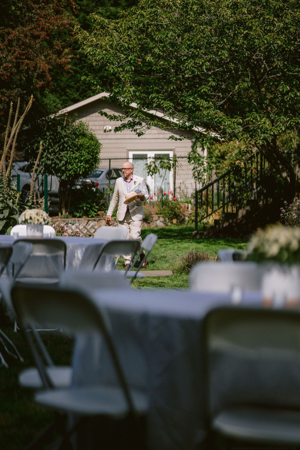 Tables and chairs set up for an outdoor event with a small house visible in the background.