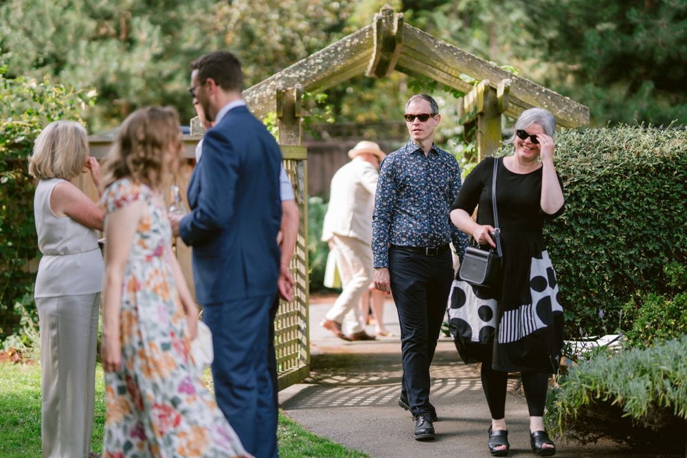 Garden party guests socializing under an arbor surrounded by landscaped grounds.