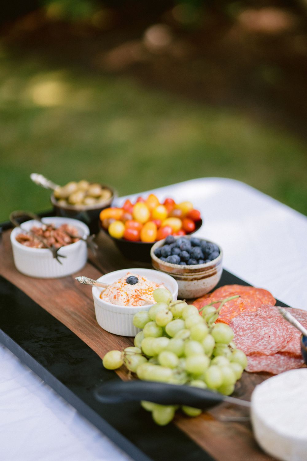 Charcuterie board with fresh fruits, meats, and nuts arranged on a wooden serving platter.