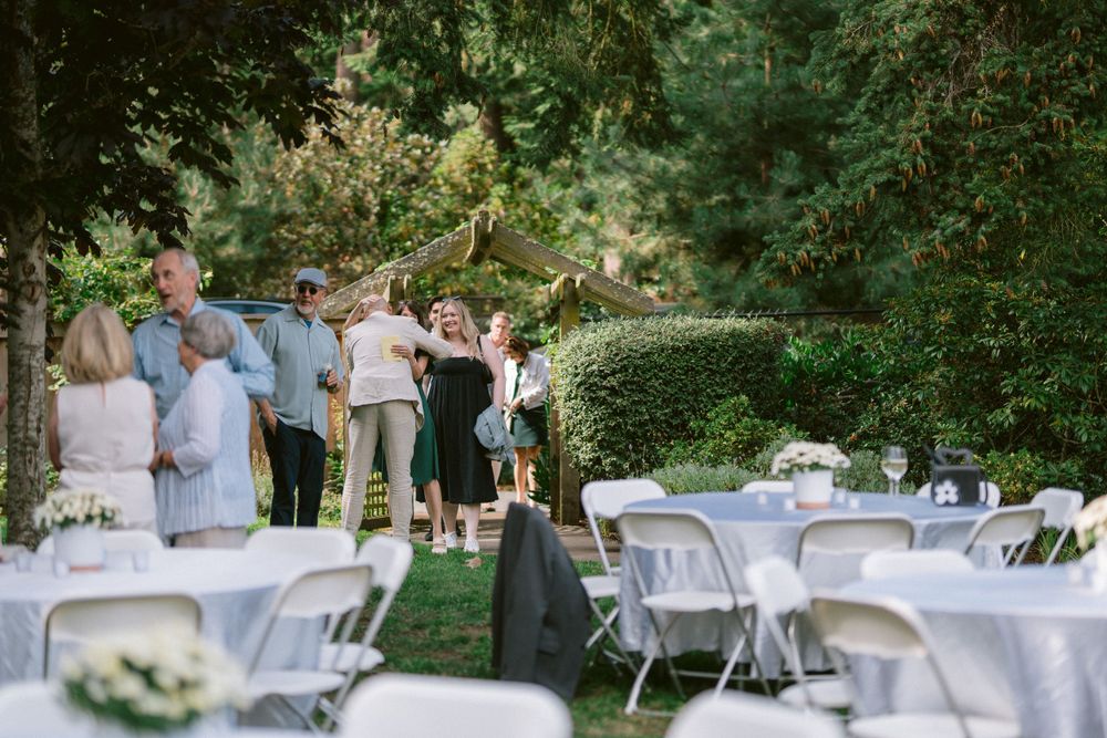 Outdoor wedding reception setup with white chairs and tables under trees.