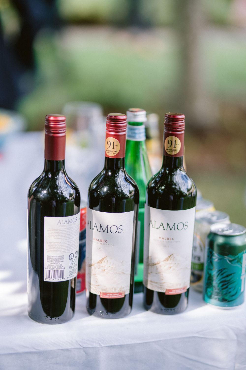 Wine bottles of Lamos brand displayed on white tablecloth at outdoor event.