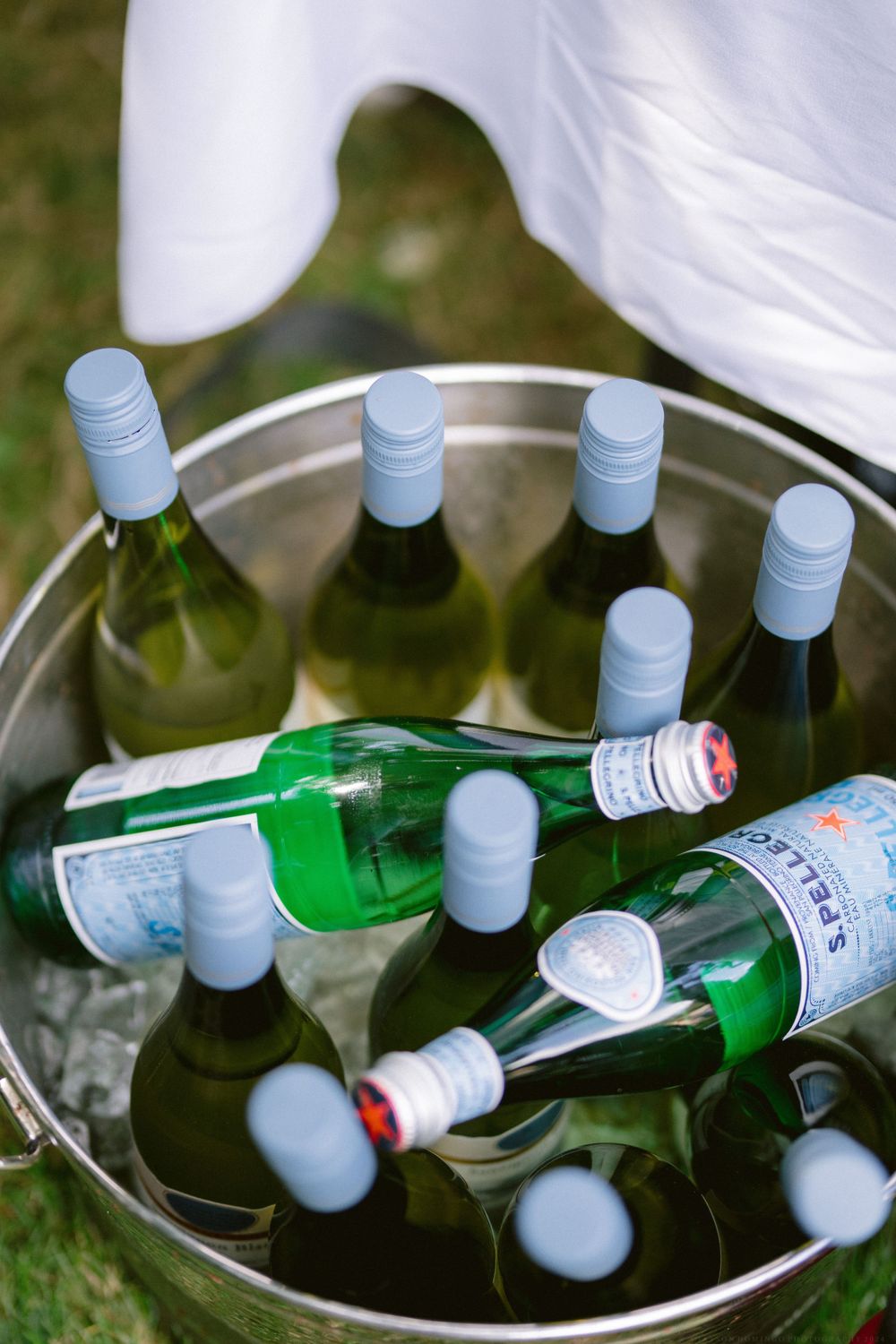 Ice bucket filled with chilled white wine bottles at outdoor party.