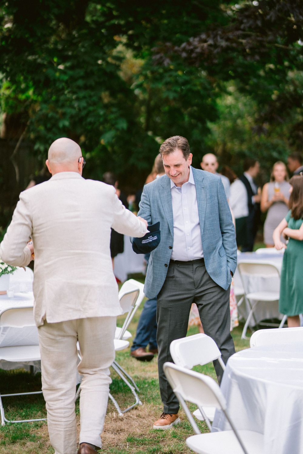 Men in formal attire greeting each other at an outdoor event with white folding chairs.