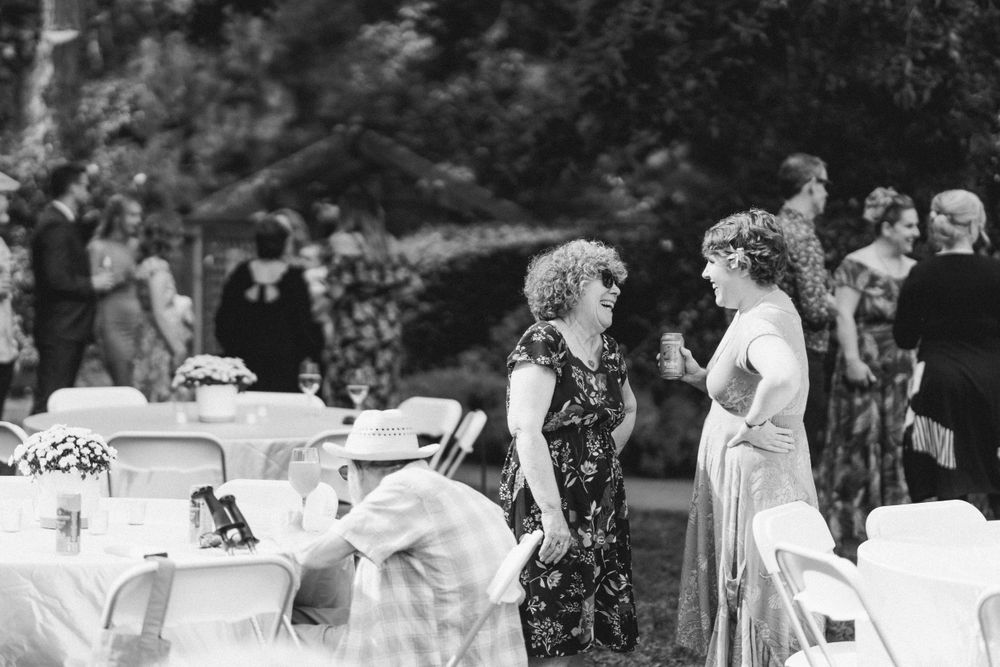 Black and white photo of guests mingling at an outdoor garden party with white tables and chairs.