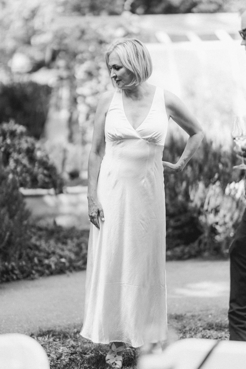 Black and white portrait of woman in elegant white dress standing in garden setting.