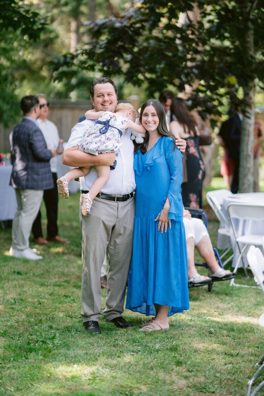 Family poses together on lawn at outdoor event with white folding chairs in background.