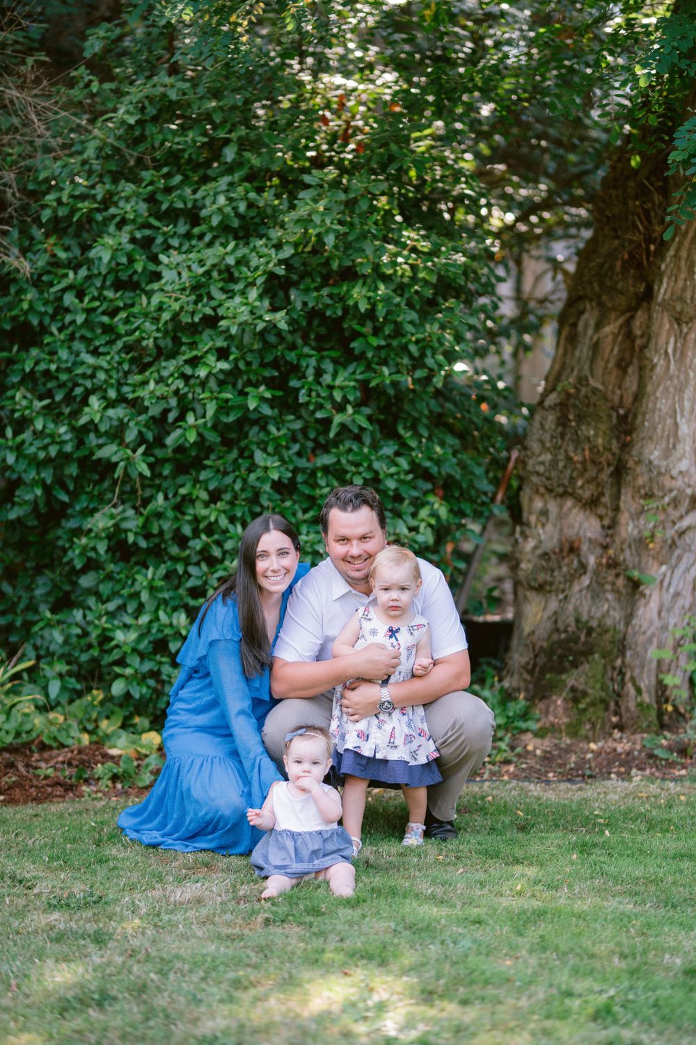 A family poses together on a lush green lawn with large trees in the background.