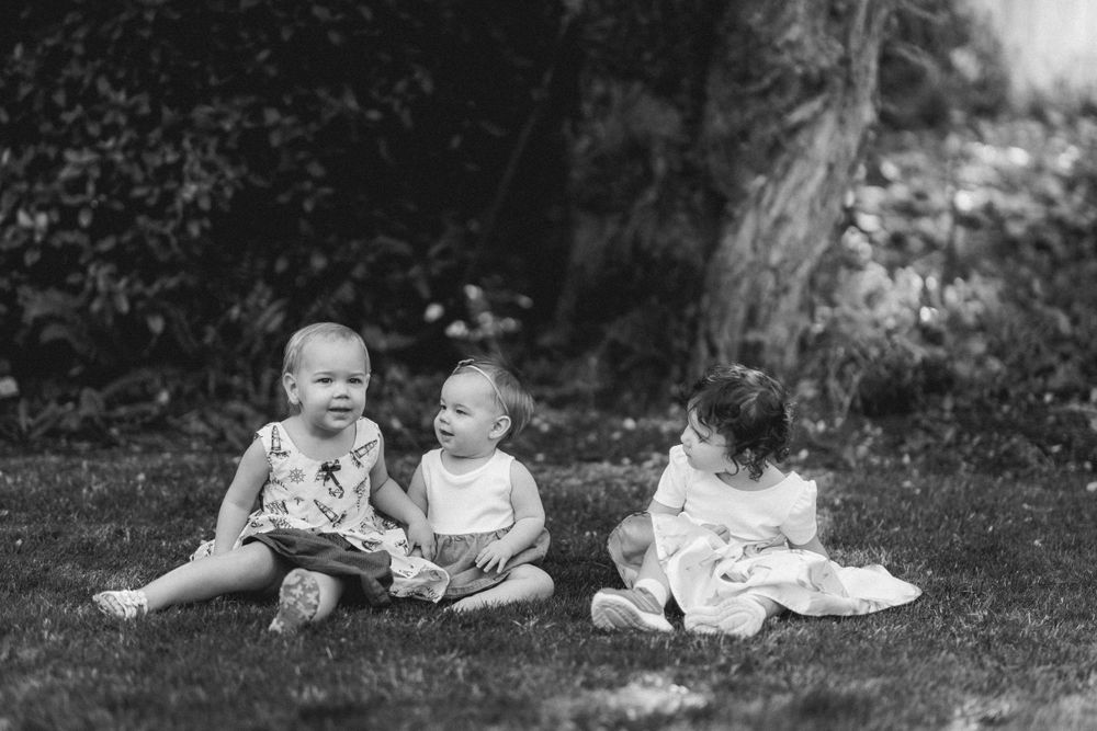 Three small children sit on grass in vintage black and white photography style.