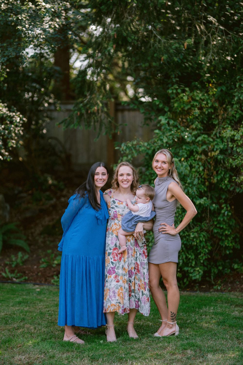 A group poses together in summer dresses against a backdrop of green foliage.