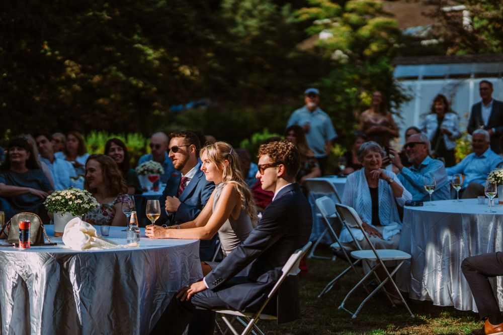 Wedding reception table setup in backyard garden with blue accents and white tablecloths.