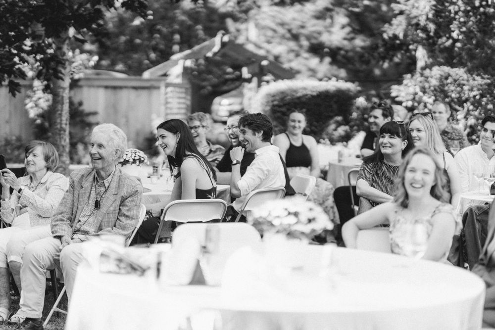 Black and white photo captures candid moments of guests enjoying outdoor celebration.