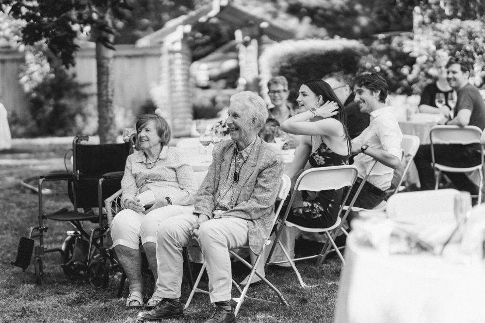 Black and white photograph of guests seated in folding chairs at outdoor gathering.