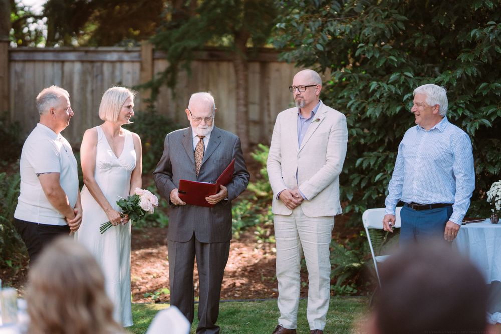 An intimate outdoor wedding ceremony taking place in a garden setting with greenery backdrop.