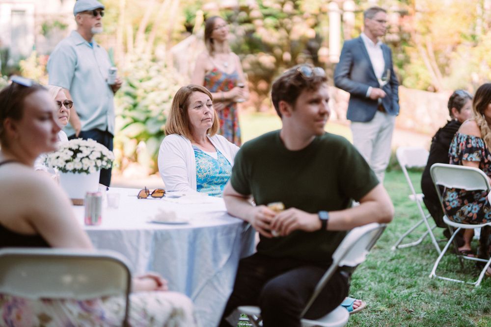 Guests seated at round tables with blue tablecloths during a casual outdoor gathering.