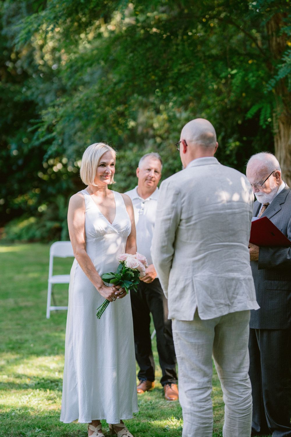 A garden wedding ceremony with participants standing on grass surrounded by trees.