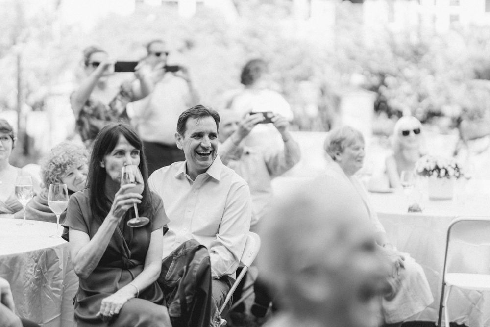 Black and white candid shot of guests enjoying drinks and laughter at an outdoor wedding reception.