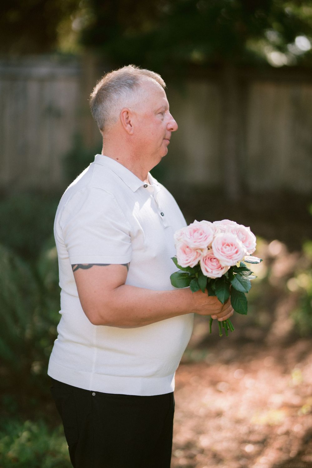 Person in white polo shirt holding pink roses bouquet in garden setting.