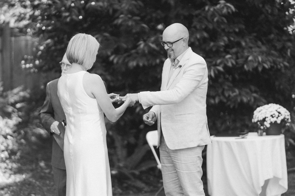 Black and white capture of wedding ceremony exchange in garden setting.