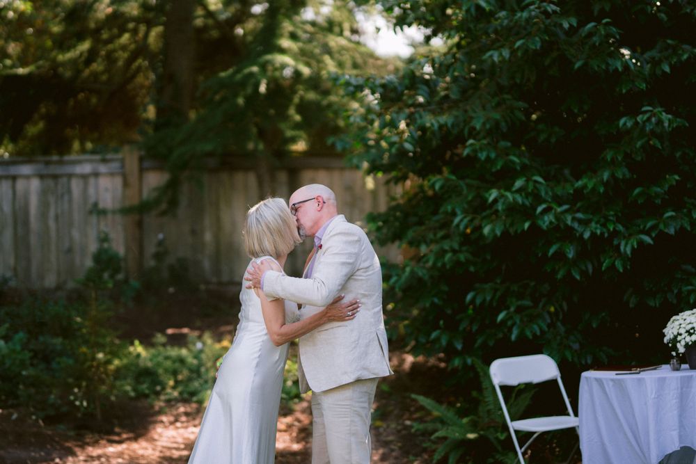 A tender kiss shared between newlyweds in a sunlit garden setting.