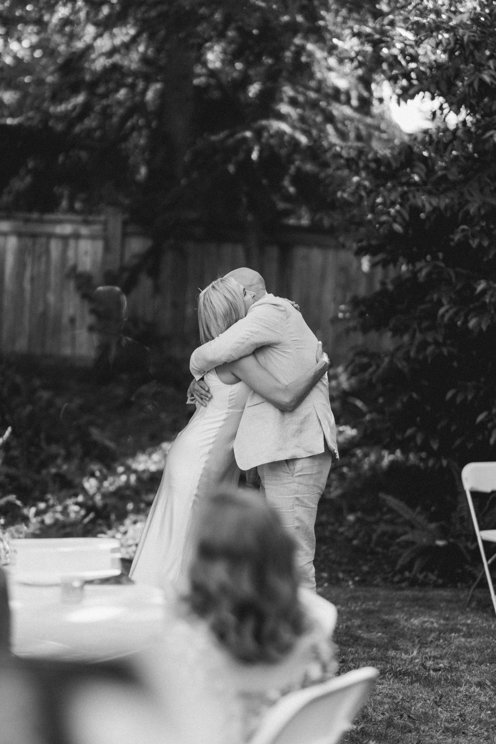 An intimate embrace between a couple in wedding attire at an outdoor garden ceremony.