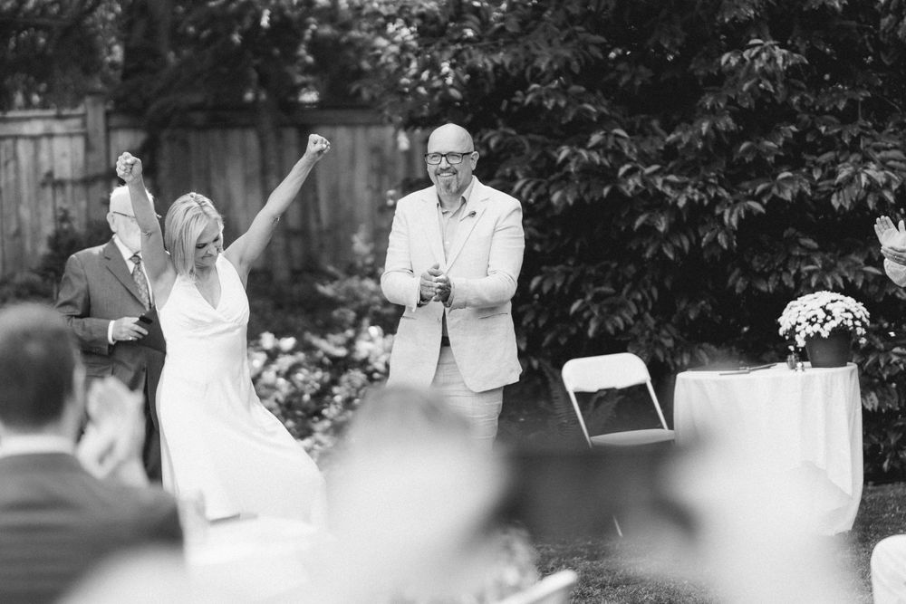 A celebratory moment during an outdoor wedding ceremony with guests seated on white chairs.