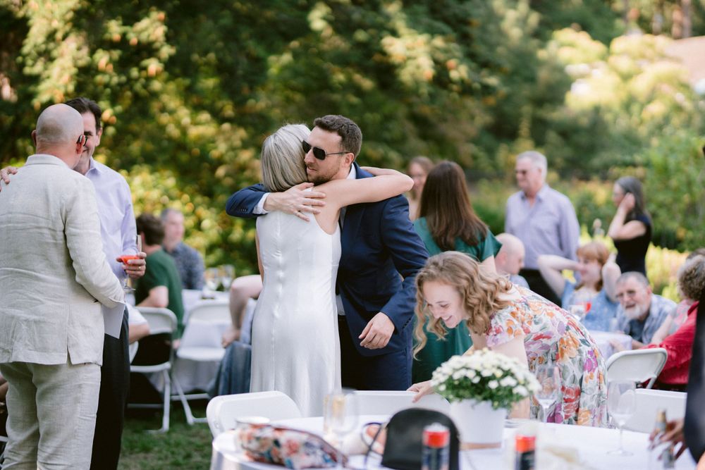 Wedding guests gather around decorated tables at an outdoor garden reception.